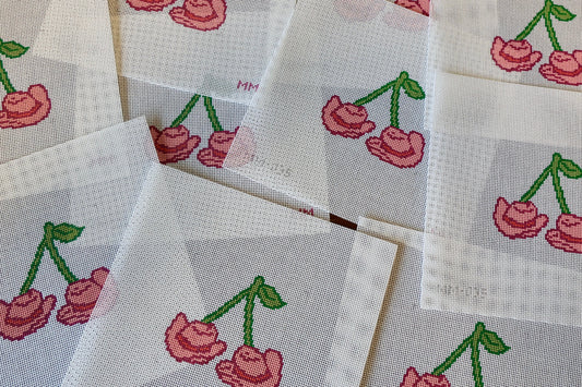 Needlepoint with cherry cowboy hat designs on a wooden surface